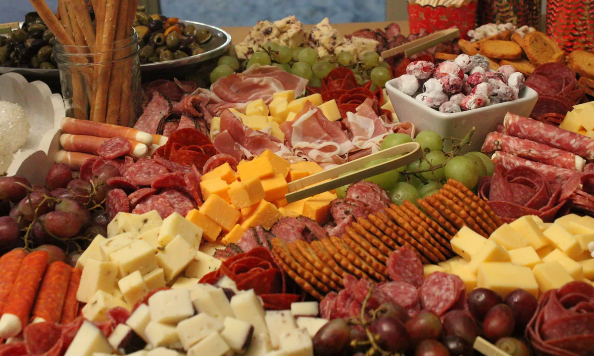 A close-up of the Christmas grazing table with cheeses, folded meats, grapes, berries and rows of crackers