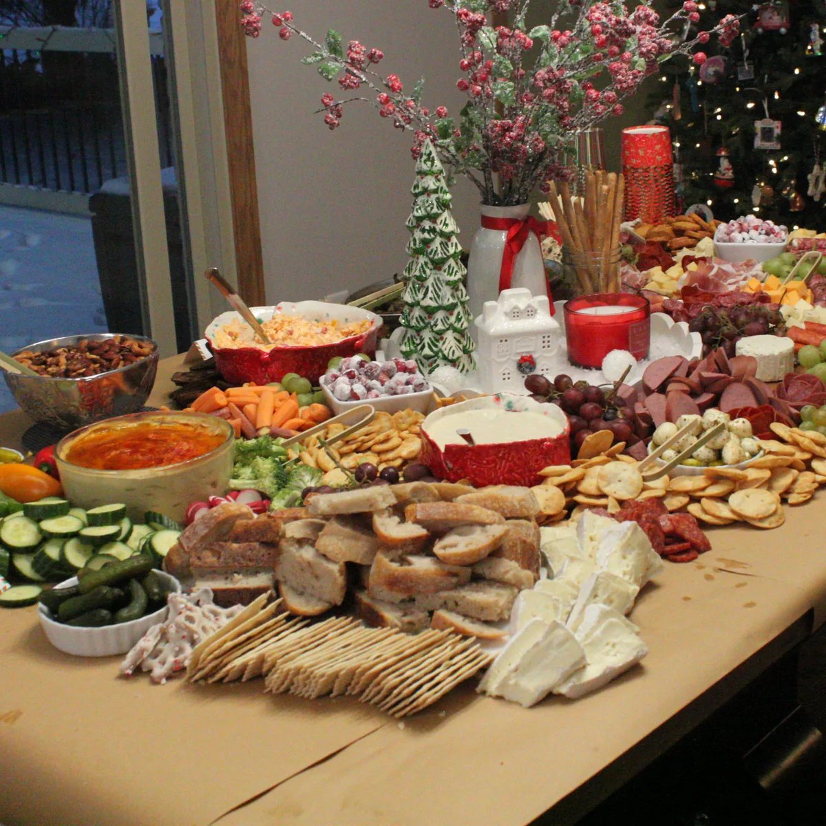 A Christmas grazing table with cheeses, meats, breads, crackers, fruit and vegetables around a festive centerpiece